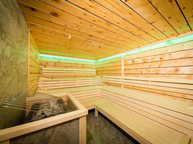 Helle Holzsauna mit Bankgestaltung, Saunaofen und grüner LED-Beleuchtung an der Decke.