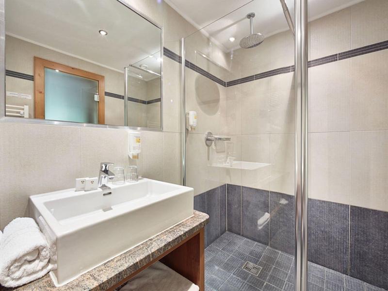 Modernes Badezimmer mit weißem Waschbecken, Glasdusche, grauen und beigen Fliesen und großem Spiegel.