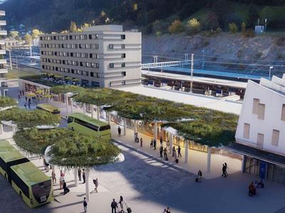 Moderner Bahnhof mit Bussen, Bahngleisen und angrenzendem mehrstöckigem Gebäudekomplex.