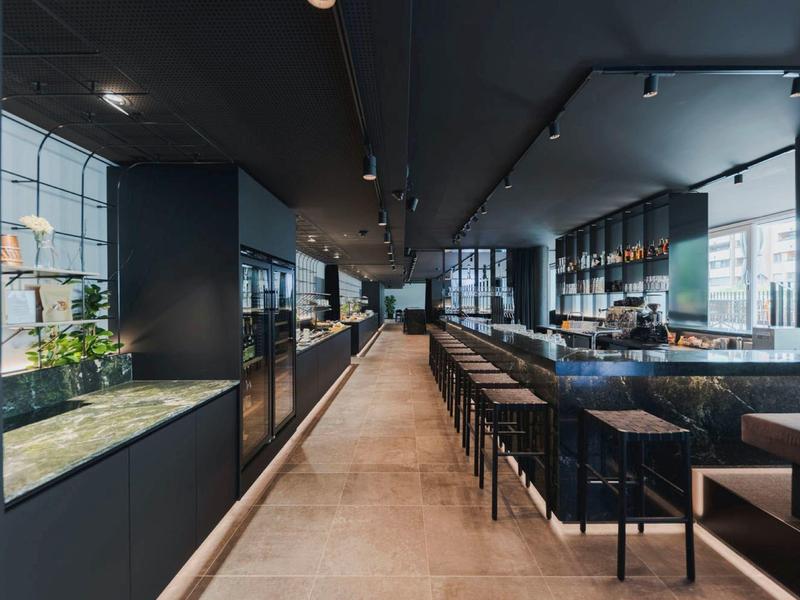 Moderní hotelový bar s vysokým stropem, černým nábytkem a velkými okny.