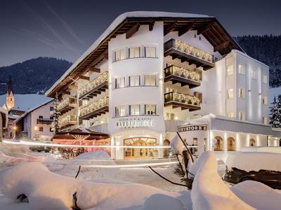 Mehrstöckiges Hotel mit Balkonen, umgeben von Schnee und Bergen im Abendlicht.