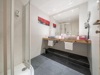 Modernes Badezimmer mit großer Spiegelwand, Doppelwaschbecken und Dusche in neutralen Farben.
