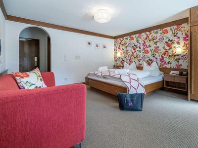 Hotelzimmer mit Doppelbett, rotem Sofa und einer bunten Blumenwand.