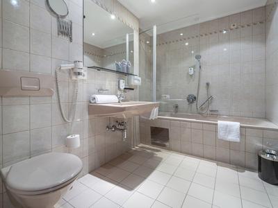 Helles Hotelbadezimmer mit Badewanne, Toilette und Waschbecken in Beige- und Grautönen.