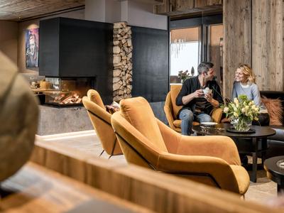 Gemütliche Hotel-Lounge mit Kamin, gelben Sessel und zwei Menschen auf dem Sofa.