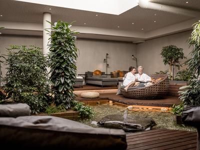 Paar entspannt auf Lounge-Sessel in Hotel-Lobby mit Pflanzen und modernem Design.