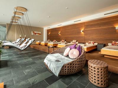 Wohnlicher Wellnessbereich mit Holzverkleidung, gepolsterten Loungesesseln und mehreren Liegen.