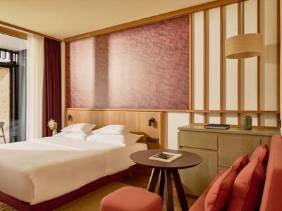 Modern eingerichtetes Hotelzimmer mit Doppelbett, rotem Sofa und Zugang zum Balkon.