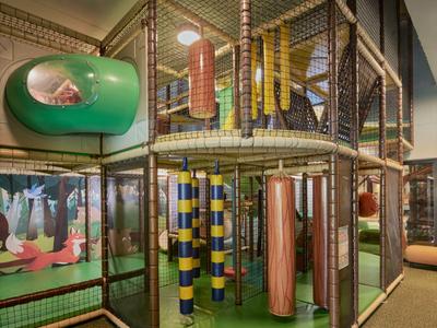 Kinder-Spielecke mit Klettergerüst und Röhrenrutsche in einem Hotelinnenbereich.