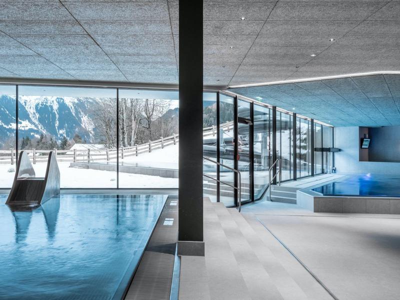 Piscina coperta moderna con scivolo e finestre panoramiche con vista sulle montagne innevate.