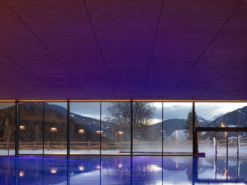 Piscina con finestre panoramiche e vista sulle montagne al crepuscolo in hotel.