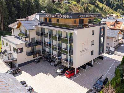 Modernes Hotelgebäude mit Balkonen, großen Fenstern und Parkplätzen, umgeben von Grünflächen.