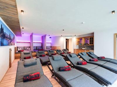 Moderner Wellnessraum mit grauen Liegen, violetter Beleuchtung und Holzdecke, hell und einladend.