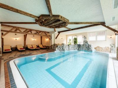 Helles Hallenbad mit Holzdeckenbalken, Liegestühlen und großen Fenstern für Tageslicht.