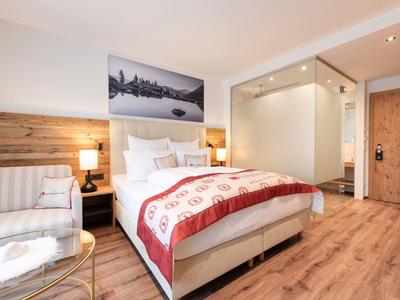 Modernes Schlafzimmer mit großem Bett, Holzfußboden, Glas-Duschkabine und gemütlicher Beleuchtung.