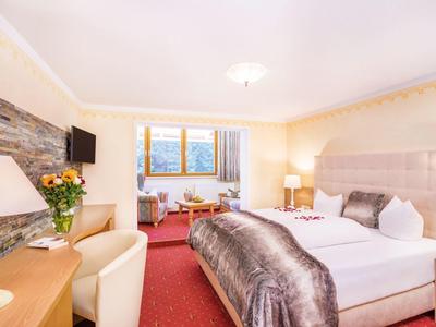 Gemütliches Hotelzimmer mit großem Bett, Teppichboden, Stühlen und Fenster mit Bergblick.