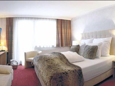 Modernes Hotelzimmer mit großem Bett, braunen Vorhängen, Teppichboden und gemütlicher Beleuchtung.