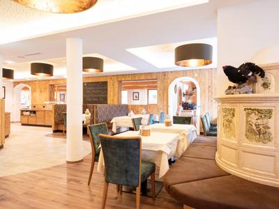 Helles Restaurant mit Holzboden, weißen Tischen, blauen Stühlen und modernen Lampen an der Decke.