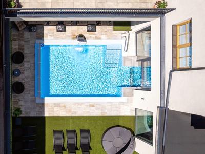 Dachterrasse mit rechteckigem Pool, Liegestühlen, rundem Sonnenschirm und künstlichem Gras.