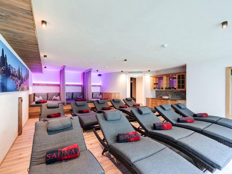 Moderner Wellnessraum mit grauen Liegen, violetter Beleuchtung und Holzdecke, hell und einladend.