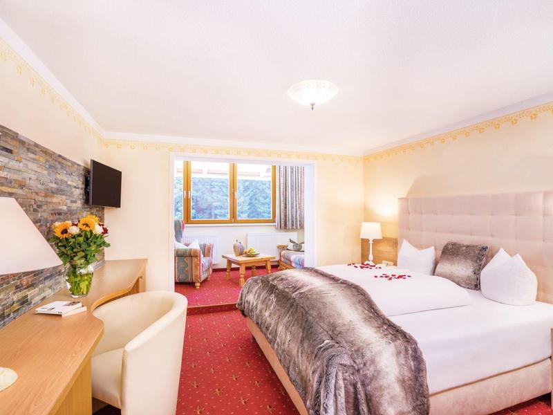 Gemütliches Hotelzimmer mit großem Bett, Teppichboden, Stühlen und Fenster mit Bergblick.