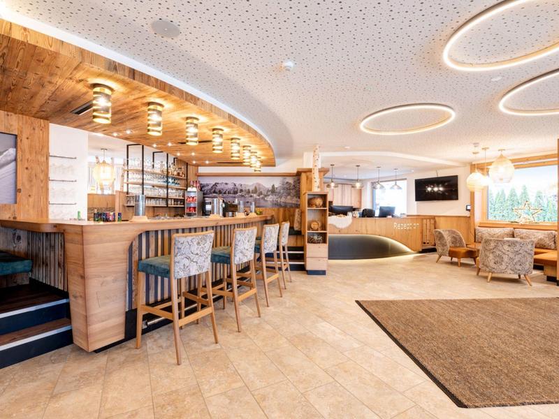 Moderner Empfangsbereich mit Holzvertäfelung, Barhockern und hellem Bodenbelag in warmem Licht.