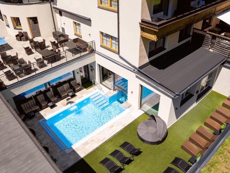 Moderner Außenbereich mit kleinem Pool, Sonnenliegen und grünem Kunstrasen an Wohngebäude.