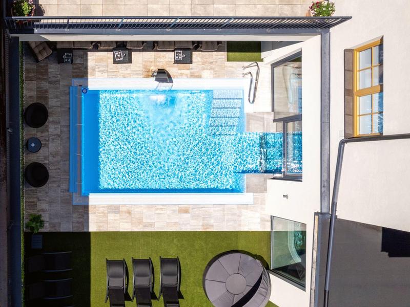 Dachterrasse mit rechteckigem Pool, Liegestühlen, rundem Sonnenschirm und künstlichem Gras.