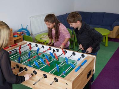 Drei Kinder spielen lebhaft an einem hellen Kicker aus Holz in einem bunten Zimmer.