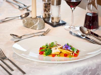 Eleganter Esstisch mit künstlerisch angerichtetem Gericht auf weißem Teller und Weinglas.