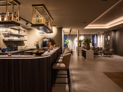 Moderne Hotelbar mit Hockern, stilvoller Beleuchtung und gemütlichem Sitzbereich im Hintergrund.