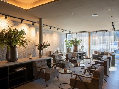 Modern eingerichteter Hotel-Loungebereich mit Sesseln, Sitzgruppen und großen Fenstern.