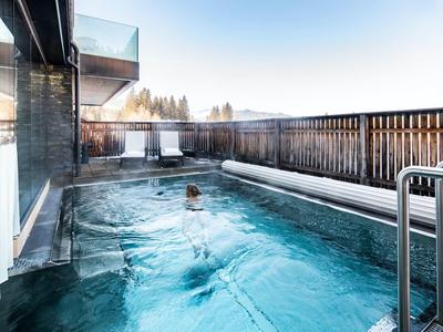 Piscina all'aperto con acqua azzurra limpida, circondata da recinzione in legno, asciugamani e sedute esterne.