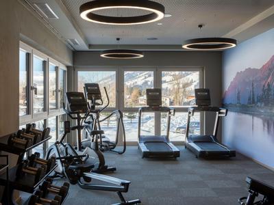 Moderner Fitnessraum mit Cardio-Geräten und Bergblick durch die großen Fenster.