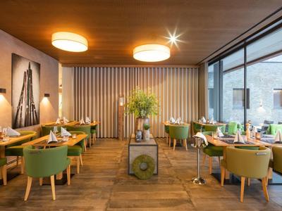 Modern interieur van het restaurant met groene stoelen, houten plafond en grote ramen naar het terras.