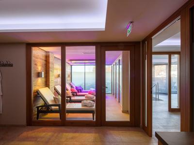 Area spa moderna con sedie a sdraio in legno e pareti di vetro che si affacciano su una stanza luminosa.