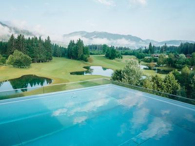 Infinity-Pool mit Blick auf einen grünen Golfplatz und bewaldete Hügel im Nebel.