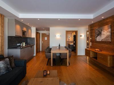 Suite d'hotel moderna con pavimenti in legno, tavolo da pranzo, cucina e area salotto accogliente.