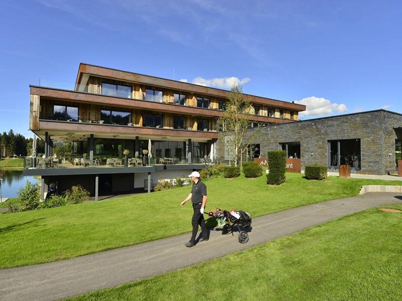 Moderno edificio dell'hotel con terrazze vicino a un lago e golfista che cammina sul prato verde.