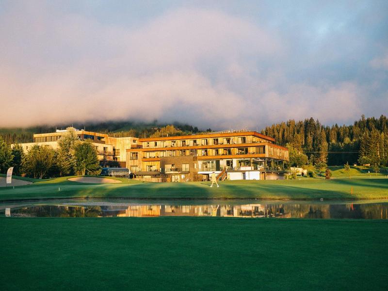 Grande hotel circondato da campi verdi e alberi sotto un cielo nuvoloso.