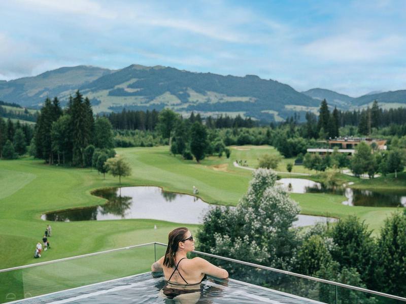 Donna si rilassa in piscina a sfioro con vista su montagne e campo da golf.