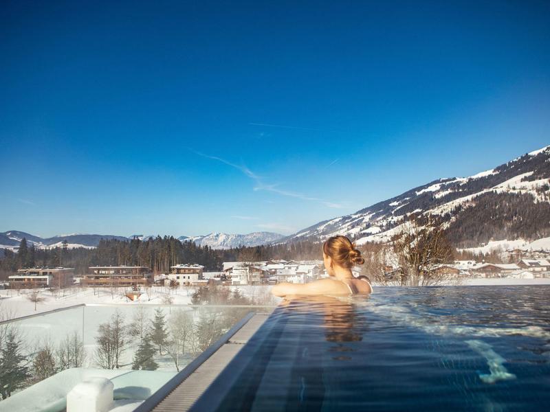Donna si rilassa in piscina all'aperto con vista sulle montagne innevate e cielo azzurro.