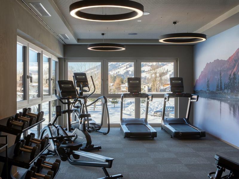 Palestra moderna con attrezzature e grandi finestre che mostrano montagne innevate.