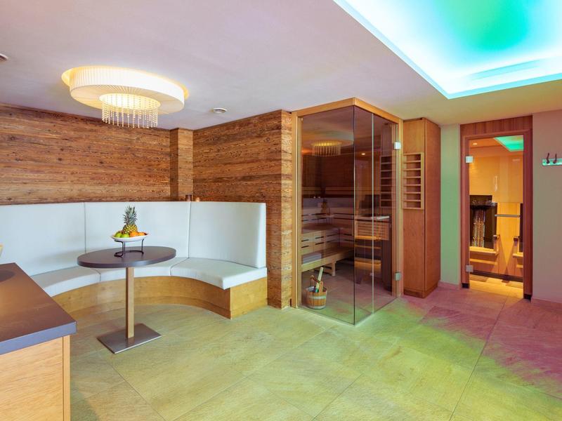 Lounge spa moderna con sauna in legno, area salotto bianca e illuminazione soffusa.