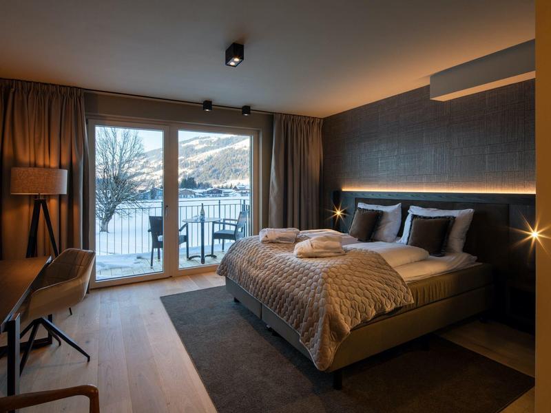 Camera d'hotel accogliente con letto matrimoniale, balcone e vista sul lago al tramonto.