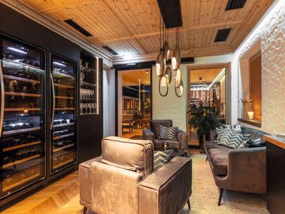 Acogedora zona de lounge con sillas de cuero y refrigeradores de vino en interior de madera iluminado cálidamente.