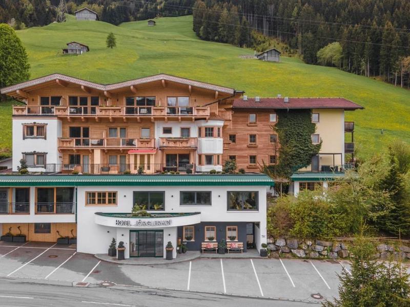 Hotel building with balconies and parking spaces in front of green hill landscape