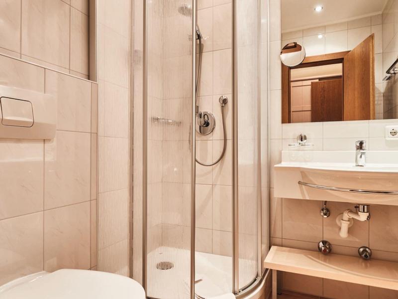 Bright hotel bathroom with curved shower cabin, toilet, and sink under a large mirror.