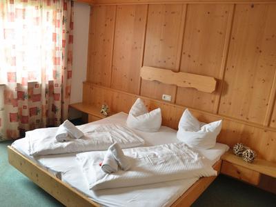 Gemütliches Hotelzimmer mit Holzwänden, Doppelbett und Fenster mit Vorhängen.