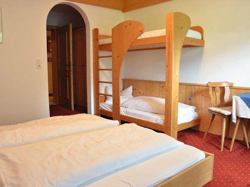 Schlafzimmer mit Etagenbett und Doppelbett, Holzmöbel, rotem Teppich und weißem Bettzeug.